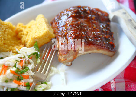 Knoblauch-Barbecue-Sauce auf Baby Back Ribs mit Maisbrot und Krautsalat auf weißem Teller Stockfoto
