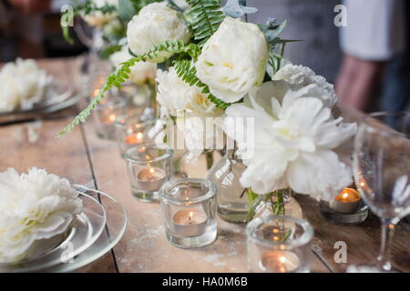 Schöne rustikale Hochzeitstafel geschmückt mit schönen weißen David Austin Rosen und Kerzen in Glashaltern. Loft-Stil Stockfoto