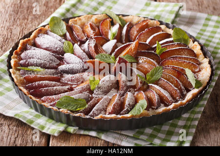 Pflaumenkuchen mit Minze und Puderzucker in Auflaufform hautnah auf einem Tisch. horizontale Stockfoto