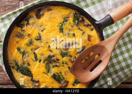 Leckeres Omelette mit Spinat, Cheddar-Käse und Pilzen in einer Pfanne Großaufnahme auf dem Tisch. Horizontale Ansicht von oben Stockfoto