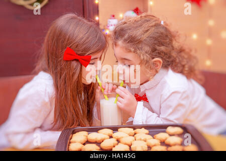 Kleine Jungen und Mädchen trinken Milch mit traditionellen festliche Lebkuchen, glückliche Kinder Weihnachtsferien genießen Stockfoto