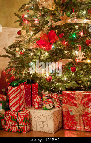 Weihnachtsgeschenke verpackt und unter hell erleuchteten Weihnachtsbaum gelegen Stockfoto