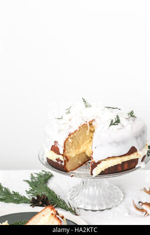 Nahaufnahme eines weihnachts-Kokos-Schwammkuchen mit Zuckerguss auf einem Kuchen neben einem Stück Kuchen auf einem Teller Stockfoto