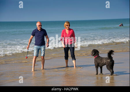 Ein reifes Paar (männlich & weiblich) das Tragen von Kleidung mit ihrem Hund Spaß an einem sonnigen Strand von Cornwall. Stockfoto