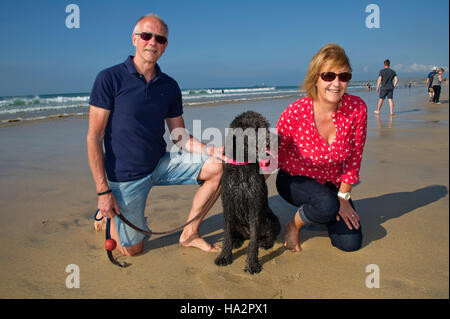 Ein reifes Paar (männlich & weiblich) das Tragen von Kleidung mit ihrem Hund Spaß an einem sonnigen Strand von Cornwall. Stockfoto