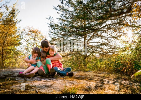 Vater sitzt im Wald drei Kinder umarmen Stockfoto