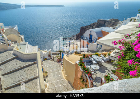 Traditionelles Santorini felsigen Architektur, mit wunderschönen Blick auf Caldera, Stufen hinunter zum Meer und kleine Taverne mit Blumen Stockfoto