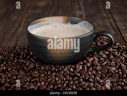 Große Tasse mit heißen Cappuccino mit Kaffeebohnen auf Holzbrett Stockfoto