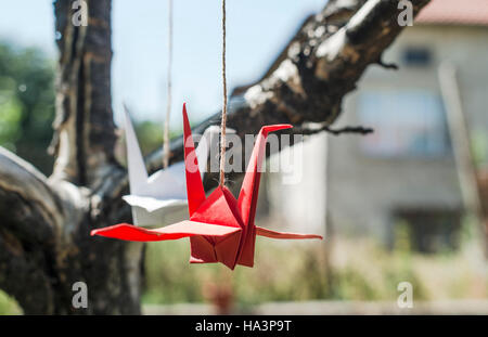 Origami-Kraniche im Garten. Figuren aus Papier in der Natur. Rote und weiße Kraniche auf Baum. Stockfoto