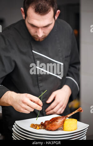 Koch macht Fleischgericht auf gewerbliche Küche Stockfoto