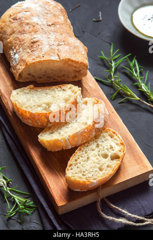 Italienisches Brot Ciabatta und Rosmarin auf schwarzem Hintergrund - frischem selbstgebackenem Brot Bäckerei Stockfoto