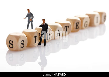 Strategie, Deutsch für Strategie, geschrieben mit Holzbuchstaben und zwei Miniaturfiguren manager Stockfoto