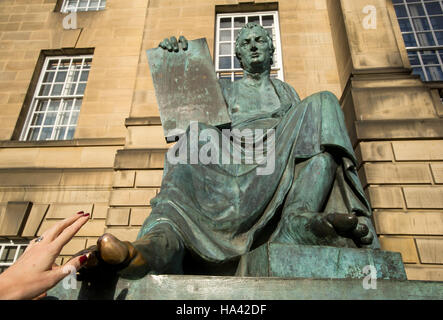 Ein Tourist berührt den großen Zeh der Statue des Philosophen David Hume außerhalb der High Court auf Edinburghs Royal Mile. Stockfoto