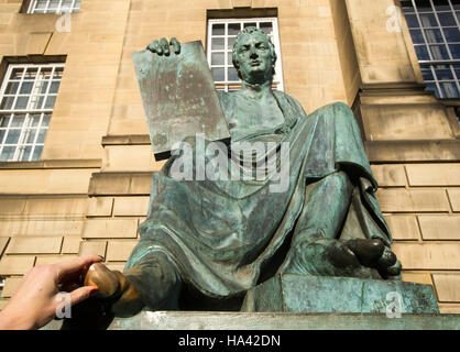 Ein Tourist berührt den großen Zeh der Statue des Philosophen David Hume außerhalb der High Court auf Edinburghs Royal Mile. Stockfoto