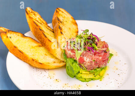 Ahi Thunfisch-Tartar gestapelt mit Avocado, Rucola, garniert mit Mikro Grüns, serviert mit gegrilltem Crostini Brot Stockfoto