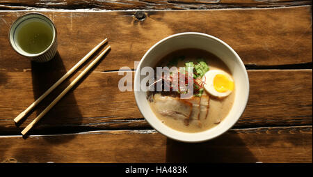 Mittags Schüssel mit japanischen Nudeln und Ramen-Brühe mit Essstäbchen und Teetasse auf rustikalem Holztisch Stockfoto