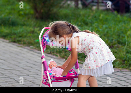 Niedliche kleine Mädchen mit ihrem Spielzeug Kutsche und Puppe im freien Stockfoto