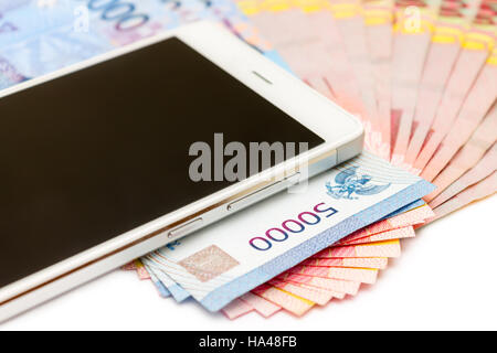 Smartphone über den Haufen von indonesische Rupiah (IDR) Banknoten auf dem weißen Hintergrund. Stockfoto