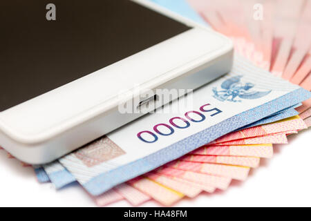 Smartphone über den Haufen von indonesische Rupiah (IDR) Banknoten auf dem weißen Hintergrund. Stockfoto