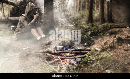 Junge, weibliche Tee zu trinken, durch das Feuer im Wald Stockfoto