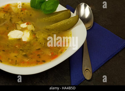 Weißer Teller mit Gurken Suppe und Creme Blot zu fördern, die frische Basilikumblätter und Scheiben Gurke, steht auf einem Stein Arbeitsplatte, blaue Serviette und Löffel Stockfoto