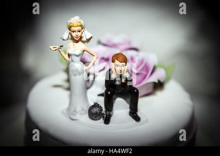 Miniatur von Braut und Bräutigam auf Hochzeit Kuchen, mit Mann mit einem Ball und Kette am Bein und Frau durch Gedrückthalten der Taste... Comic-Konzept der Eheversprechen Stockfoto