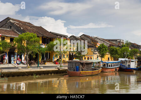 Holzboote am Thu Bon Fluss in Hoi An Ancient Town (Hoian), Vietnam. Gelbe alte Häuser am Wasser. Stockfoto