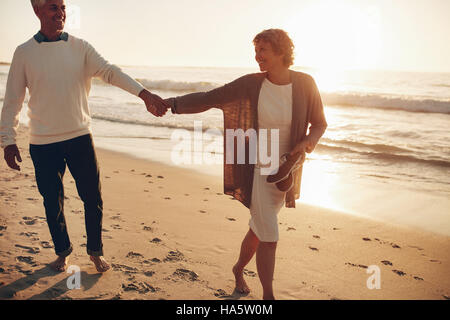 Im Freien Schuss des romantischen älteres paar zu Fuß entlang der Küste, die Hand in Hand. Ältere Mann und Frau zusammen spazieren am Strand bei Sonnenuntergang. Stockfoto