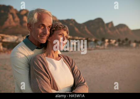 Porträt von älteren Ehepaar zusammenstehen und umarmt am Strand. Ältere Mann umarmt seine schöne Frau und Weg betrachten. Stockfoto