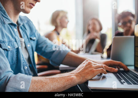 Schuss von junger Mann mit Laptop mit Klassenkameraden im Hintergrund studieren hautnah. Schüler lernen in der Universitätsbibliothek. Stockfoto
