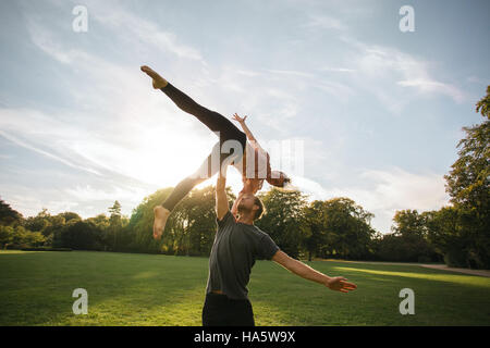 Mann und Frau paar Yoga im Freien in einem Park zu tun. Passen Sie junges Paar üben Acroyoga. Mann heben und Frau auf der einen Seite balancieren. Stockfoto