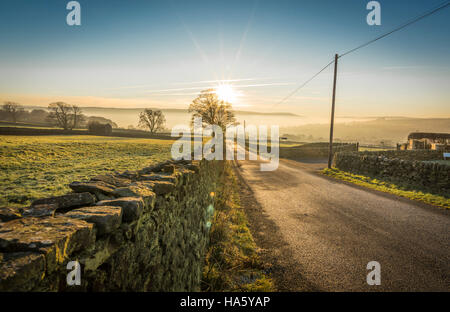 Die Sonne, die Einstellung über ein neblig Aire-Tal in der Nähe von Silsden und Keighley, West Yorkshire, im Winter 2016 Stockfoto