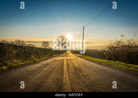 Die Sonne, die Einstellung über ein neblig Aire-Tal in der Nähe von Silsden und Keighley, West Yorkshire, im Winter 2016 Stockfoto