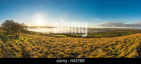 Die Sonne, die Einstellung über ein neblig Aire-Tal in der Nähe von Silsden und Keighley, West Yorkshire, im Winter 2016 Stockfoto