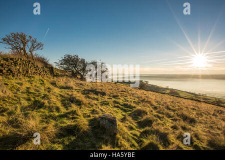 Die Sonne, die Einstellung über ein neblig Aire-Tal in der Nähe von Silsden und Keighley, West Yorkshire, im Winter 2016 Stockfoto