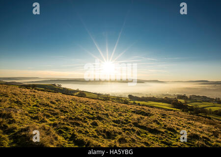 Die Sonne, die Einstellung über ein neblig Aire-Tal in der Nähe von Silsden und Keighley, West Yorkshire, im Winter 2016 Stockfoto