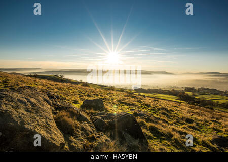 Die Sonne, die Einstellung über ein neblig Aire-Tal in der Nähe von Silsden und Keighley, West Yorkshire, im Winter 2016 Stockfoto