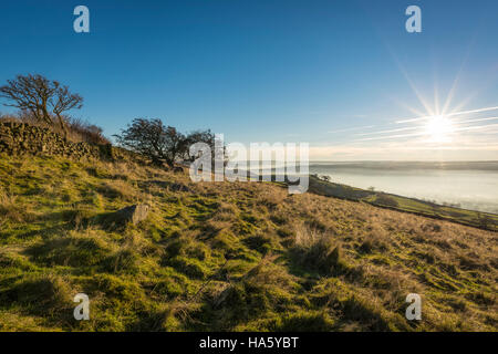 Die Sonne, die Einstellung über ein neblig Aire-Tal in der Nähe von Silsden und Keighley, West Yorkshire, im Winter 2016 Stockfoto