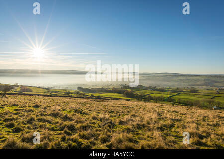 Die Sonne, die Einstellung über ein neblig Aire-Tal in der Nähe von Silsden und Keighley, West Yorkshire, im Winter 2016 Stockfoto