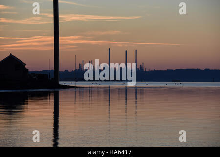 Pembroke-Raffinerie in einem Sonnenuntergang Silhouette. Spiegelt sich in ruhigem Wasser mit orange Wolken und blauer Himmel Stockfoto