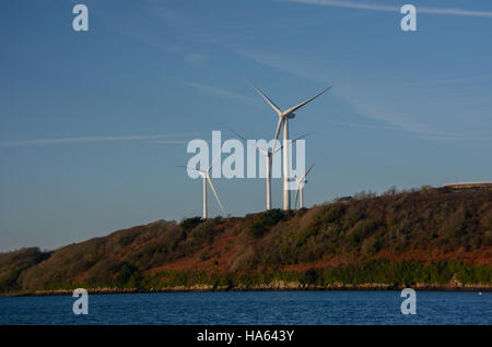 Windkraftanlagen vor blauem Himmel mit Strähnen von Zirruswolken. Küstenlinie von grünen und braunen Vegetation mit ruhigen tiefen blauen Meer Stockfoto