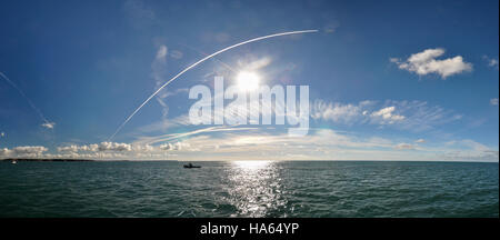 Ein Boot motorisch über eine ruhige türkisfarbene Meer unter einem blauen Himmel mit Wolken und Kondensstreifen am Eingang zum Milford Haven Stockfoto