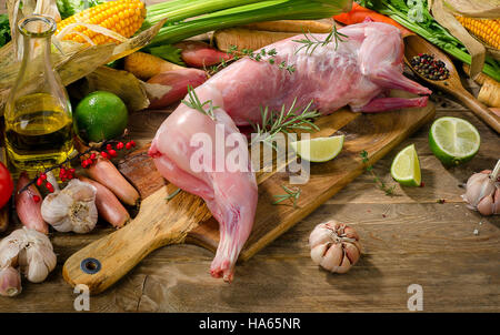 Rohe ganzes Kaninchen mit Gemüse und frischen Kräutern auf hölzernen Hintergrund. Stockfoto