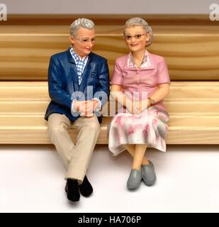 Ein älterer senior Miniatur Figur paar sitzt auf einer Holzbank Stockfoto