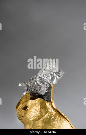 Schoko Osterhase, eingehüllt in glänzenden goldenen und silbernen Aluminium-Folie, knabberte teilweise entfernt, Folie gerissen offen an die Spitze Stockfoto