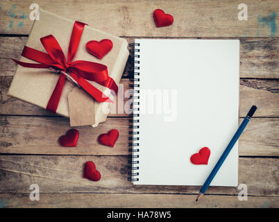 Draufsicht (oben) Geschenk-Box und rotes Band und rotes Herz mit Notebook zum Valentinstag auf Tisch aus Holz. Valentine Hintergrund. Stockfoto