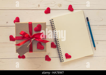 Draufsicht (oben) Geschenk-Box und rotes Band und rotes Herz mit Notebook zum Valentinstag auf Tisch aus Holz. Valentine Hintergrund. Stockfoto