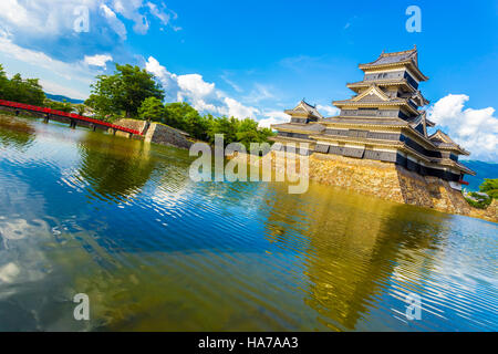 Schräge Ansicht von Matsumoto Castle, rote Brücke und Wassergraben Wasserreflexion am blauen Himmel Tag in der Präfektur Nagano, Japan Stockfoto