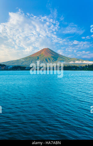 Zentriert den Fuji badet im Morgenlicht Seite während Lake Kawaguchiko im Schatten unter bewölkten blauen Himmel an einem Sommertag sitzt Stockfoto