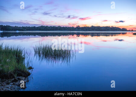 Sonnenuntergang über einer ruhigen Bucht mit Gras, Reflexionen und reichlich Farbe Stockfoto